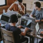 A group of professionals at a table, using laptops to discuss AI management tools and their impact on workplace efficiency.