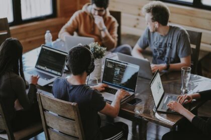 A group of professionals at a table, using laptops to discuss AI management tools and their impact on workplace efficiency.